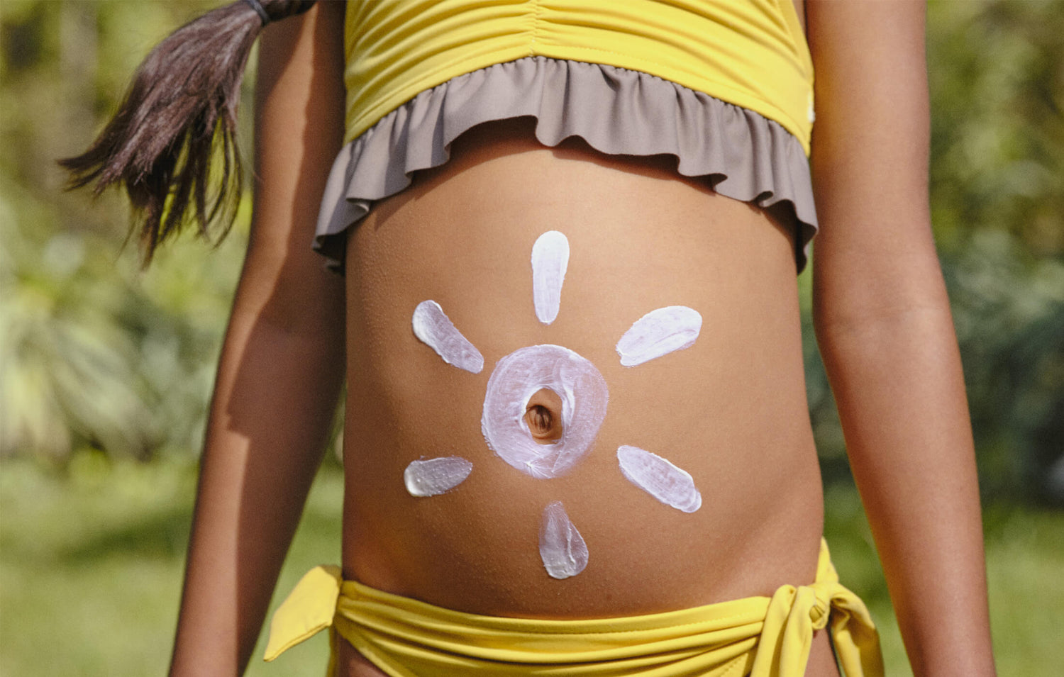 Kid drawing a sun using sunscreen on her belly.